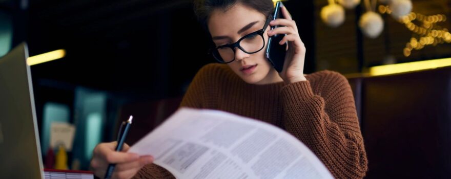 A woman is sitting at a table with papers and talking on the phone.